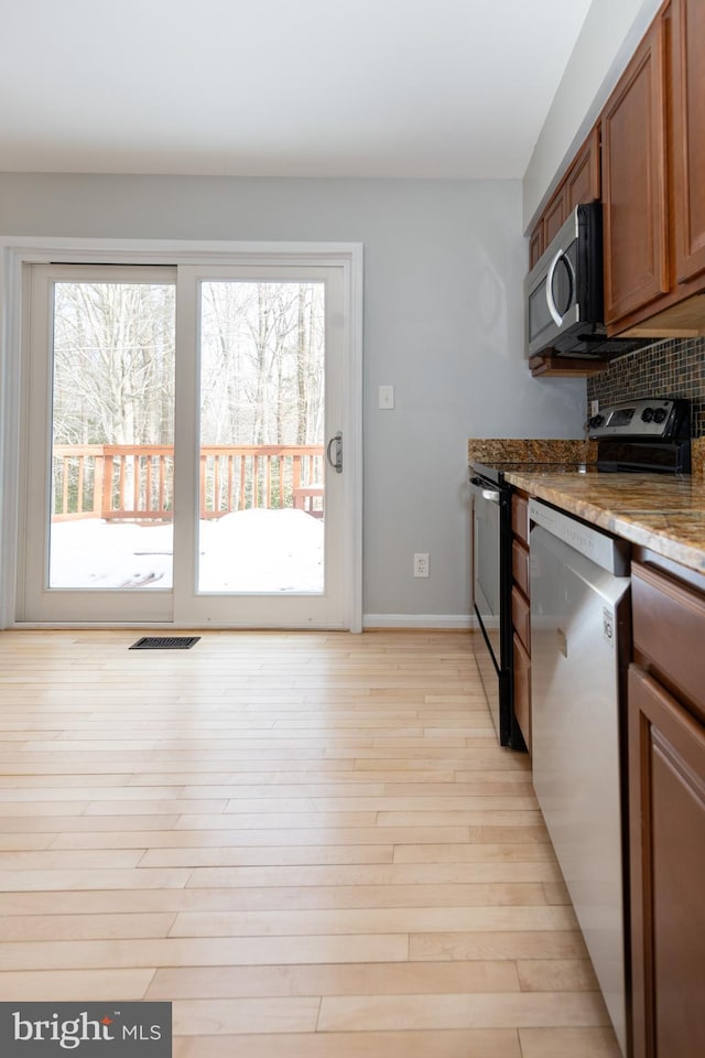 kitchen with appliances with stainless steel finishes, backsplash, light stone counters, and light hardwood / wood-style floors