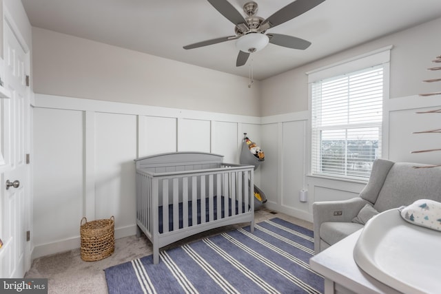 carpeted bedroom featuring ceiling fan, a crib, and multiple windows