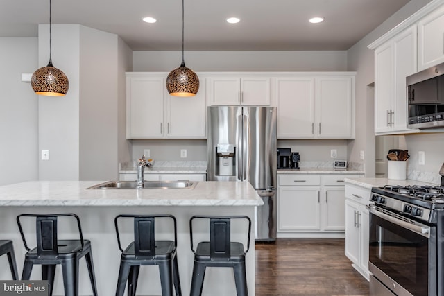 kitchen with appliances with stainless steel finishes, a kitchen island with sink, decorative light fixtures, light stone countertops, and sink