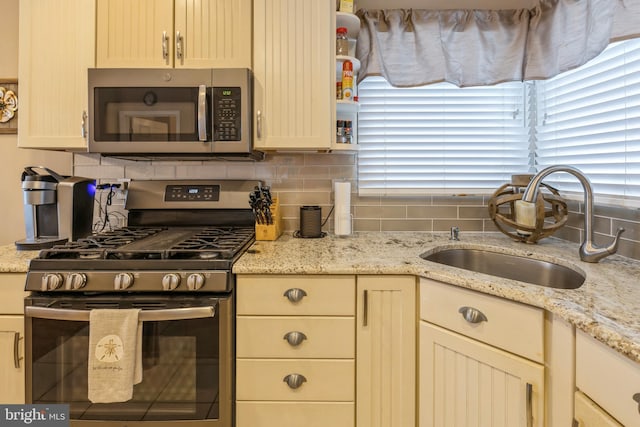 kitchen with appliances with stainless steel finishes, decorative backsplash, light stone counters, cream cabinets, and sink