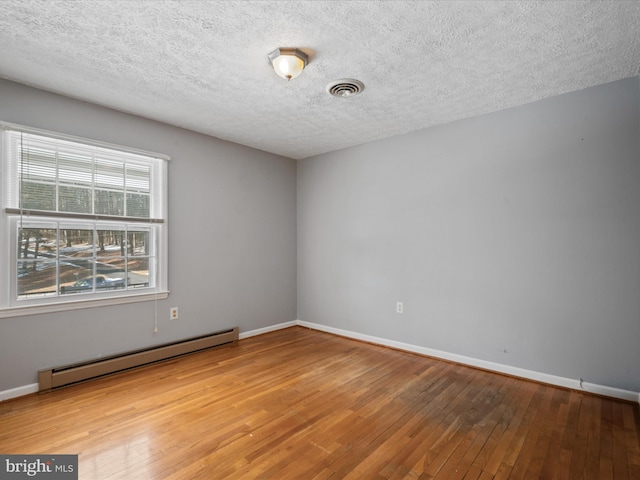 unfurnished room featuring hardwood / wood-style floors, baseboard heating, and a textured ceiling