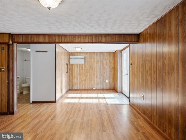 interior space featuring a textured ceiling, wooden walls, and light hardwood / wood-style flooring