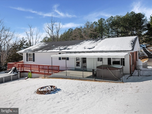 snow covered rear of property featuring a fire pit, a wooden deck, and a hot tub