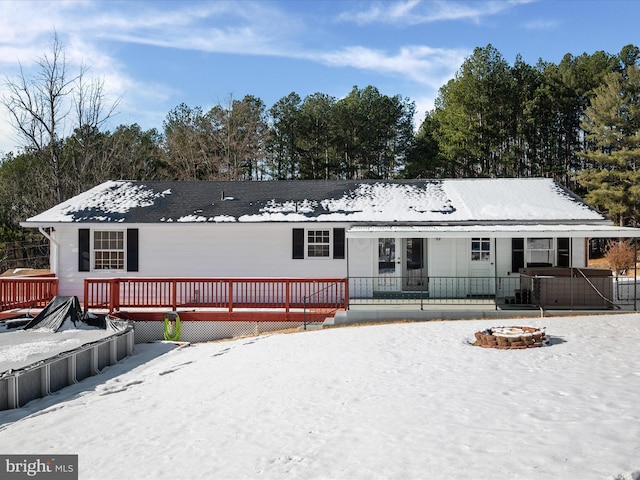 snow covered rear of property with a deck and a fire pit