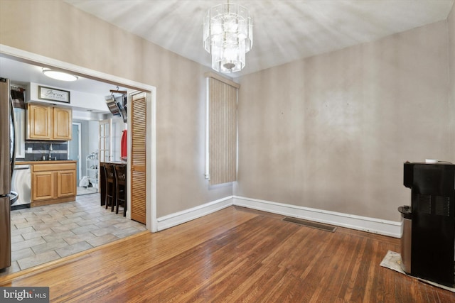 unfurnished dining area with light wood-type flooring, sink, and a chandelier