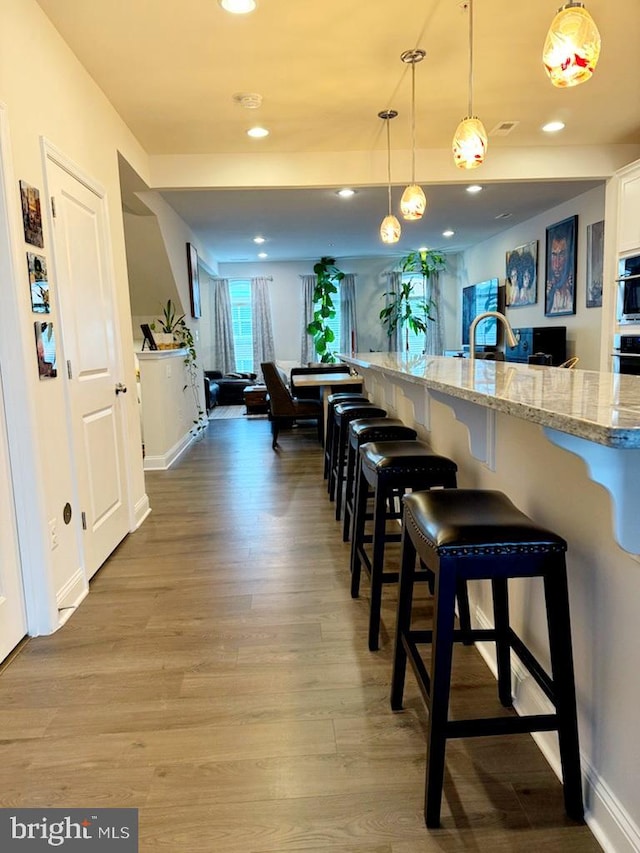 kitchen with a breakfast bar, white cabinetry, hardwood / wood-style flooring, pendant lighting, and light stone countertops