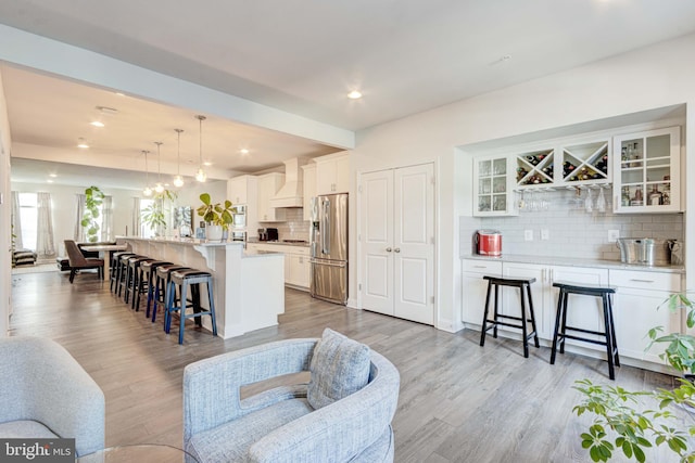 kitchen featuring pendant lighting, white cabinetry, stainless steel fridge, a kitchen bar, and a center island with sink