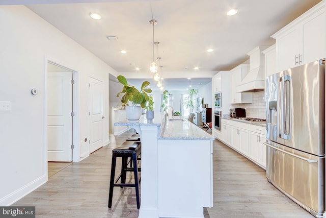 kitchen featuring stainless steel appliances, decorative light fixtures, a center island with sink, and white cabinets