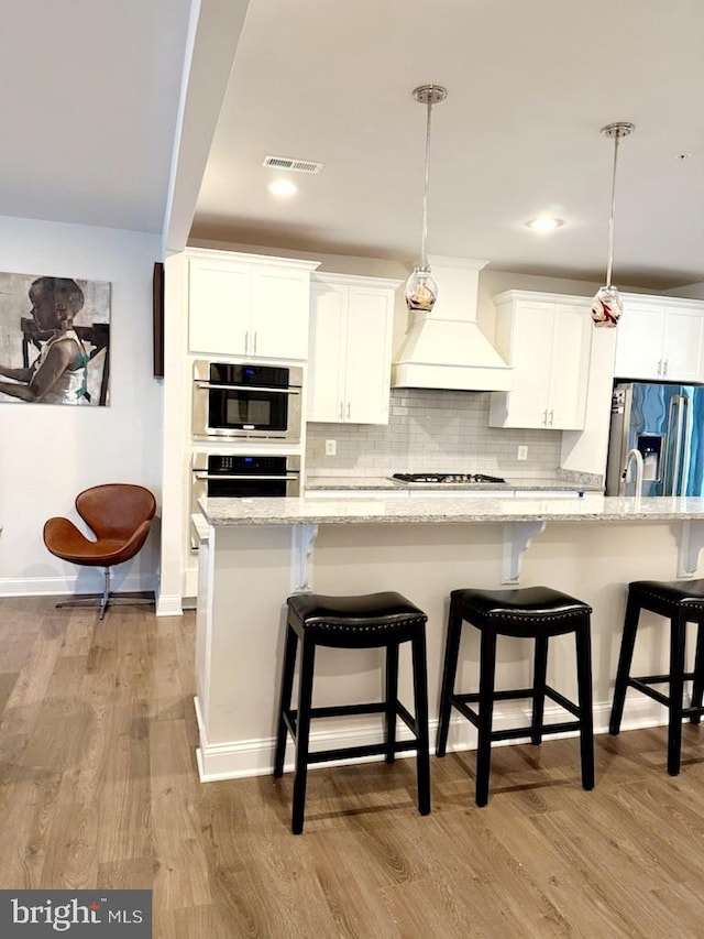 kitchen with white cabinetry, decorative light fixtures, custom exhaust hood, and stainless steel appliances