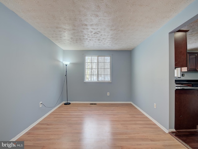 unfurnished room with light wood-type flooring and a textured ceiling