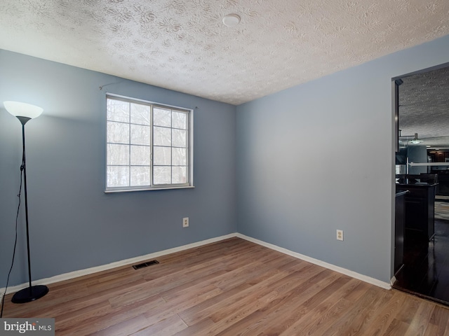 empty room with light wood-type flooring and a textured ceiling