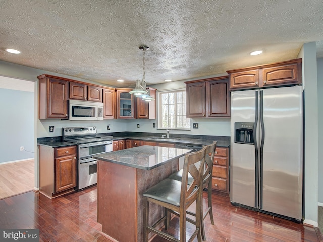 kitchen with a kitchen island, dark wood-type flooring, hanging light fixtures, and stainless steel appliances