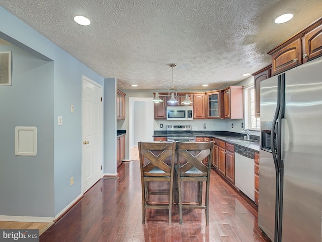 kitchen with sink, a kitchen island, pendant lighting, dark hardwood / wood-style flooring, and stainless steel appliances