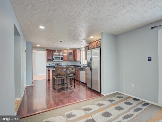 kitchen with pendant lighting, appliances with stainless steel finishes, a textured ceiling, a center island, and a breakfast bar