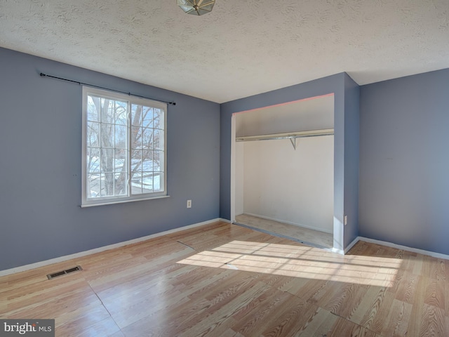 unfurnished bedroom with light hardwood / wood-style floors, a textured ceiling, and a closet