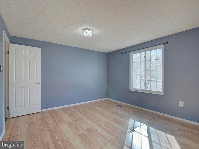 empty room with light wood-type flooring and a textured ceiling