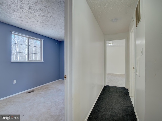 corridor featuring a textured ceiling and carpet