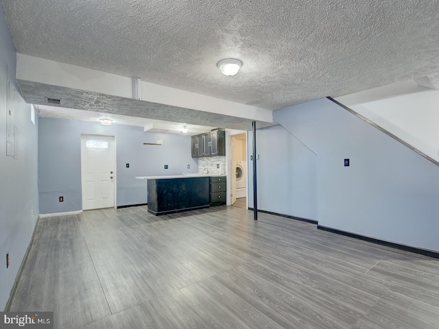 interior space with light wood-type flooring, washer / clothes dryer, and a textured ceiling