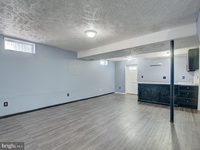 basement with sink, light wood-type flooring, and a textured ceiling