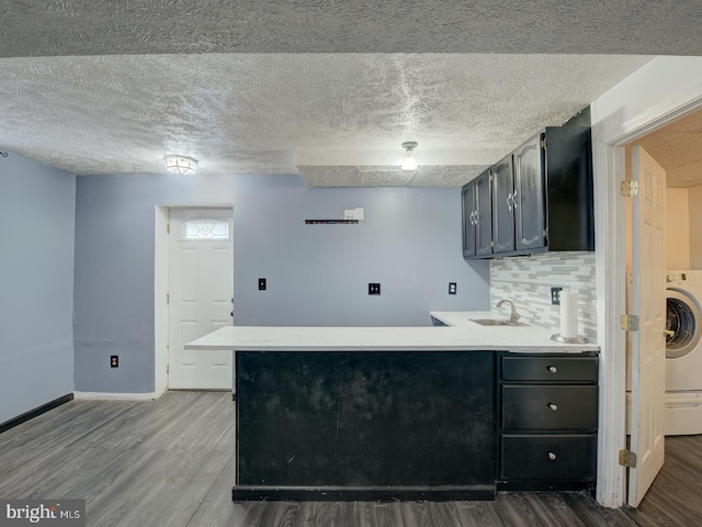 kitchen featuring kitchen peninsula, sink, washer / clothes dryer, dark hardwood / wood-style floors, and decorative backsplash