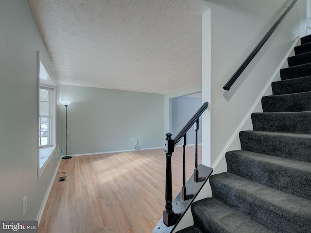 staircase with hardwood / wood-style floors and a textured ceiling