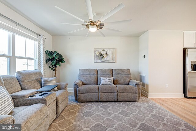 living room featuring light wood-type flooring, visible vents, baseboards, and a ceiling fan