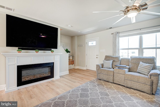 living area with visible vents, a ceiling fan, wood finished floors, a glass covered fireplace, and baseboards