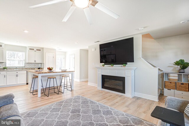 living room with a glass covered fireplace, light wood-style flooring, baseboards, and visible vents