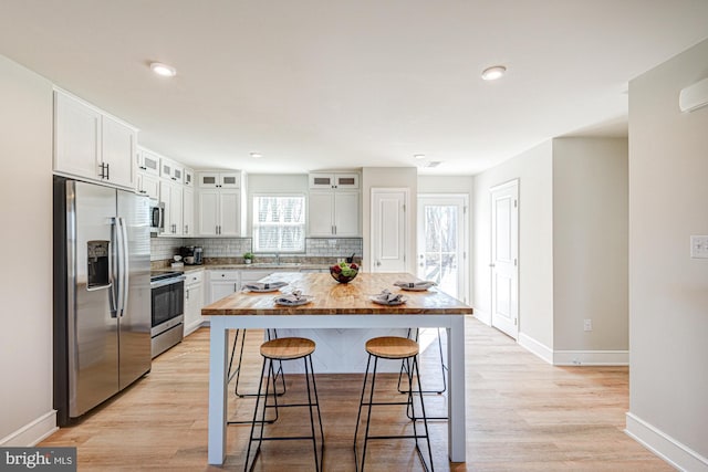 kitchen with light wood finished floors, a breakfast bar, decorative backsplash, white cabinets, and stainless steel appliances