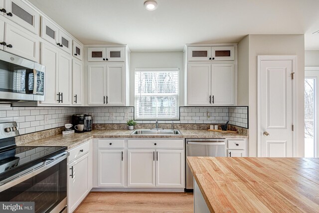 kitchen with a sink, wood counters, stainless steel appliances, white cabinets, and light wood finished floors