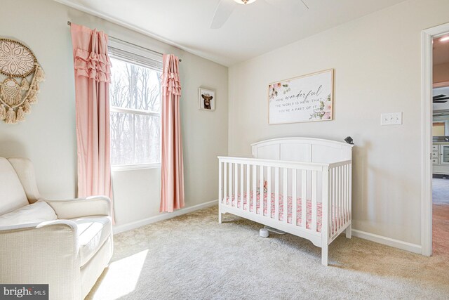 carpeted bedroom with baseboards, a nursery area, and ceiling fan