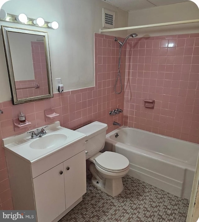 full bathroom featuring tile walls, vanity, tiled shower / bath, tile patterned floors, and toilet