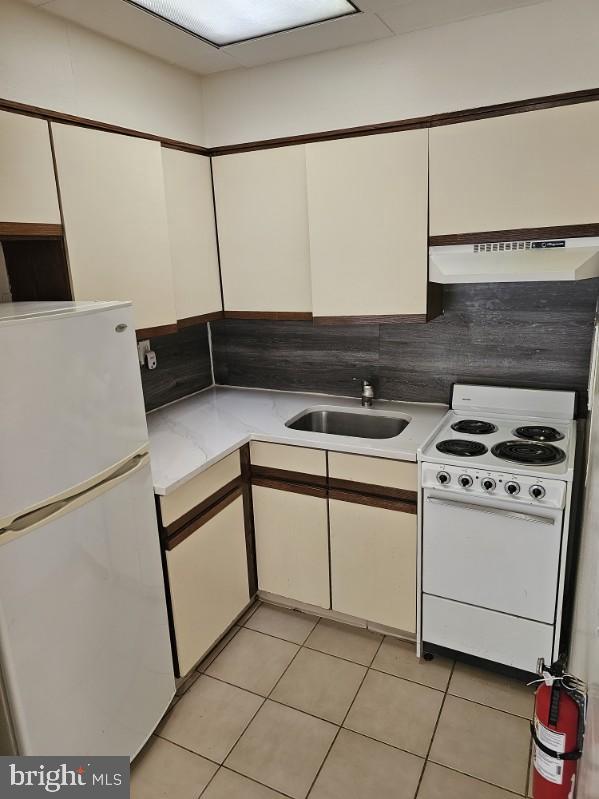 kitchen with sink, white appliances, light tile patterned floors, white cabinetry, and backsplash