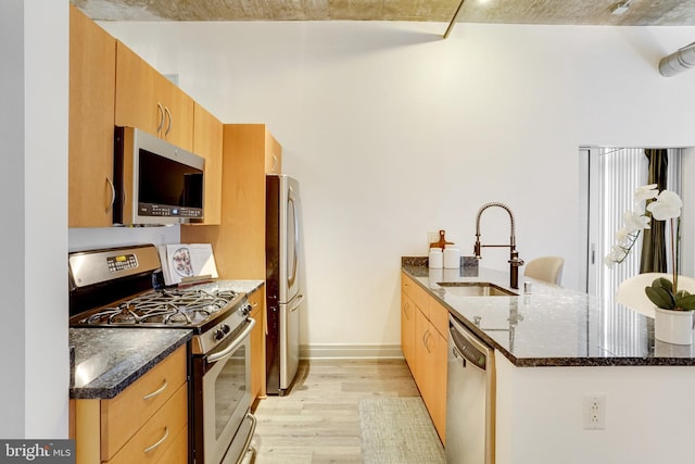 kitchen featuring appliances with stainless steel finishes, dark stone counters, sink, kitchen peninsula, and light wood-type flooring