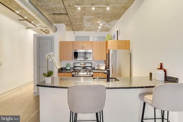 kitchen featuring light wood-type flooring, a kitchen bar, dark stone countertops, and stainless steel appliances