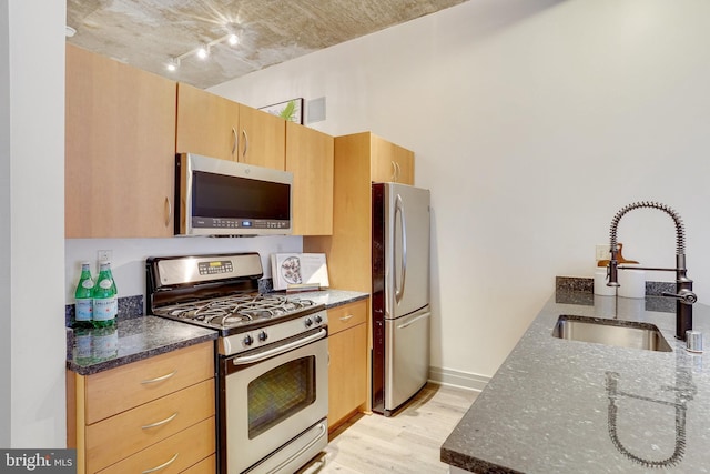 kitchen featuring light hardwood / wood-style floors, stainless steel appliances, light brown cabinetry, dark stone counters, and sink