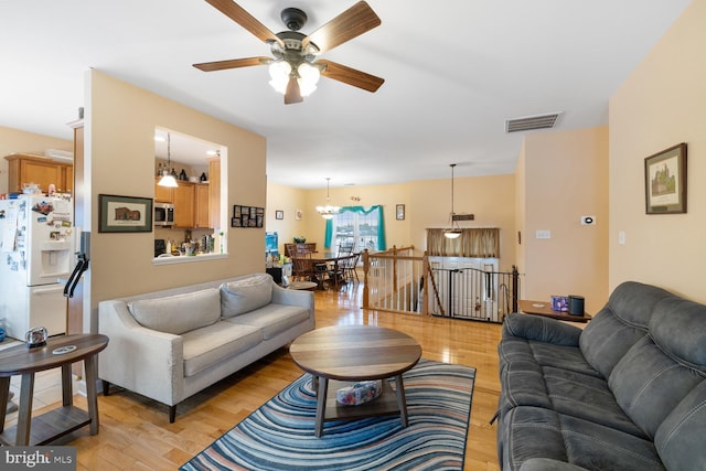 living room featuring ceiling fan with notable chandelier and light hardwood / wood-style floors