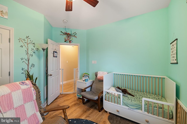 bedroom with a crib, hardwood / wood-style floors, and ceiling fan