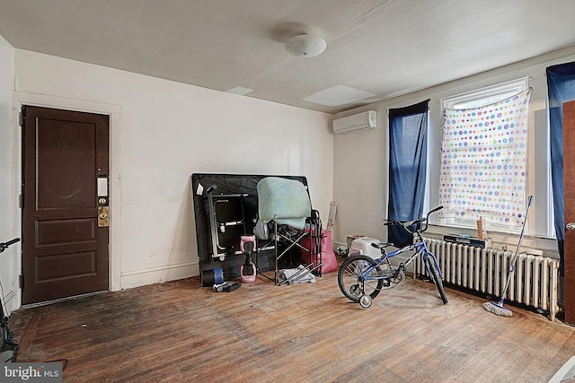 playroom with radiator heating unit, baseboards, wood finished floors, and a wall mounted air conditioner