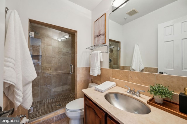 bathroom featuring tile walls, toilet, a shower with door, and vanity