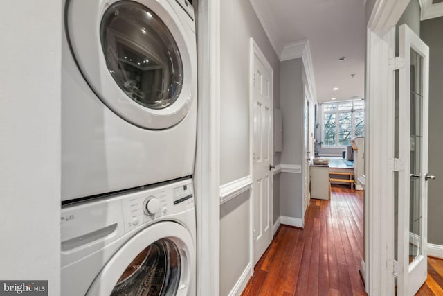 clothes washing area with stacked washer and clothes dryer, ornamental molding, and dark wood-type flooring