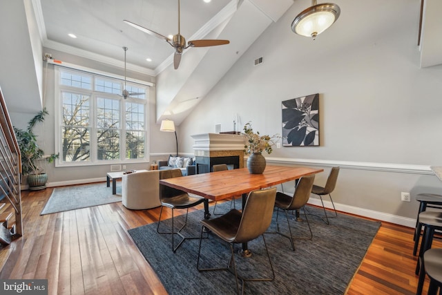 dining area featuring ceiling fan, hardwood / wood-style floors, ornamental molding, and a towering ceiling