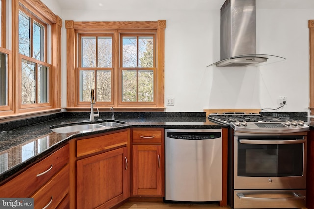 kitchen featuring dark stone countertops, appliances with stainless steel finishes, sink, and wall chimney exhaust hood