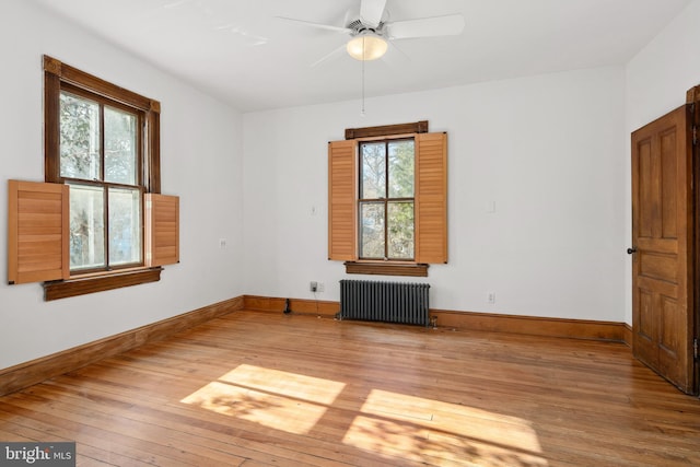 empty room featuring hardwood / wood-style flooring, radiator heating unit, and ceiling fan