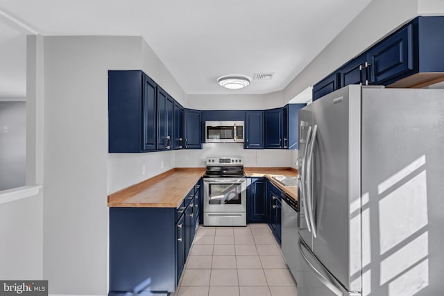 kitchen featuring light tile patterned floors, stainless steel appliances, blue cabinetry, and wooden counters