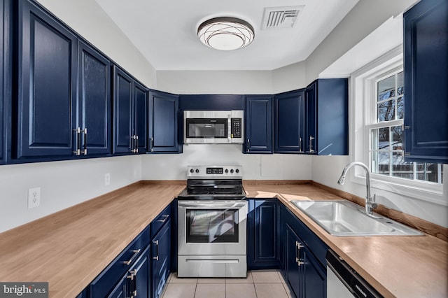 kitchen featuring wood counters, light tile patterned floors, stainless steel appliances, blue cabinetry, and sink