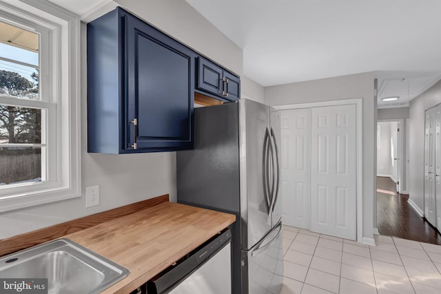 kitchen with light tile patterned floors, stainless steel appliances, blue cabinets, and wooden counters