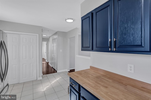 kitchen with blue cabinetry, stainless steel fridge, and light tile patterned floors