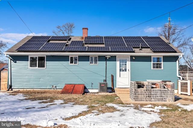 snow covered back of property featuring cooling unit and solar panels