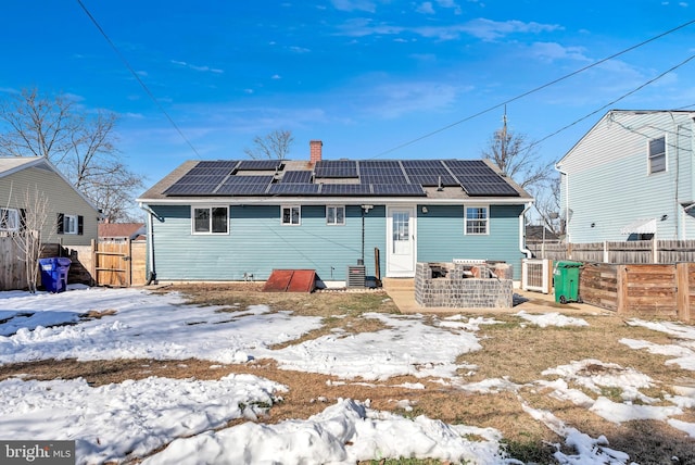 snow covered back of property featuring solar panels